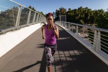 Fit afrikanisch-amerikanische Frau läuft auf Fußgängerbrücke und trainiert in der Stadt. gesunder aktiver Lebensstil und Outdoor-Fitness. — Stockfoto