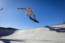 Белый мужчина прыгает и катается на скейтборде в солнечный день. тусоваться в городском скейтпарке летом. — стоковое фото