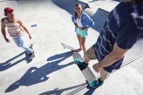Trois heureux amis caucasiens féminins et masculins skateboard au soleil. traîner dans un skatepark urbain en été. — Photo de stock