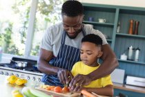 Padre e hijo afroamericanos en la cocina, cocinando juntos. en casa en aislamiento durante el bloqueo de cuarentena. - foto de stock