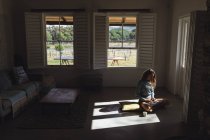 Щаслива біла жінка сидить на підлозі, використовуючи ноутбук у сонячній вітальні. просте життя в сітці сільський будинок . — стокове фото