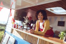 Ritratto di donna sorridente di razza mista appoggiata al bancone nel camion del cibo. concetto indipendente di business e street food. — Foto stock