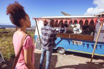 Улыбающийся африканский американец в фургоне с едой принимает заказ от клиента-мужчины. независимая концепция обслуживания бизнеса и уличной еды. — стоковое фото