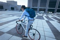 Homme d'affaires asiatique à vélo dans la rue de la ville avec des bâtiments modernes en arrière-plan. homme d'affaires dans le concept de la ville. — Photo de stock
