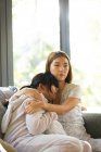 Portrait de femme asiatique sérieuse avec sa fille embrassant assis sur le canapé. à domicile en isolement pendant le confinement en quarantaine. — Photo de stock