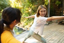 Smiling asian woman and her daughter practicing yoga on terrace in garden. at home in isolation during quarantine lockdown. — Stock Photo
