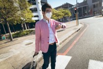Asian businessman wearing face mask walking with suitcase crossing city street. business travel out and about in city during covid 19 pandemic concept. — Stock Photo