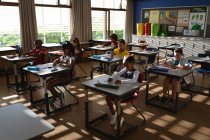 Разнообразная группа учащихся, сидящих на рабочем столе в классе начальной школы. школа и концепция образования — стоковое фото