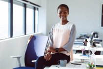 Mulher de negócios afro-americana sorridente sentada na mesa de trabalho. negócio criativo independente em um escritório moderno. — Fotografia de Stock