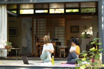 Asiatin und ihre Tochter praktizieren Yoga mit Laptop auf der Terrasse im Garten. Zuhause in Isolation während der Quarantäne. — Stockfoto