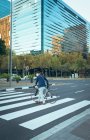 Азиатский бизнесмен в маске пересекает городскую улицу с современными зданиями на заднем плане. бизнесмен в городе во время covid 19 пандемической концепции. — стоковое фото