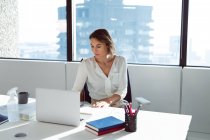 Donna d'affari caucasica seduta alla scrivania, che usa il portatile al lavoro. attività creativa indipendente in un ufficio moderno. — Foto stock