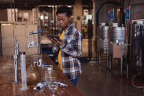 Travailleuse afro-américaine utilisant une tablette numérique à la distillerie de gin. concept de production et filtration d'alcool — Photo de stock