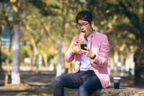 Asian businessman using smartphone drinking takeaway coffee crossing city street. digital nomad out and about in city concept. — Stock Photo