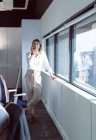Donna d'affari caucasica in piedi alla finestra, parlando con lo smartphone al lavoro. attività creativa indipendente in un ufficio moderno — Foto stock