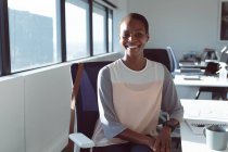 Улыбающаяся африканская американская деловая женщина, сидящая за столом на работе. независимый творческий бизнес в современном офисе. — стоковое фото
