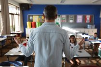 Rückansicht eines kaukasischen männlichen Lehrers, der verschiedene Schüler in der Klasse der Grundschule unterrichtet. Schul- und Bildungskonzept — Stockfoto