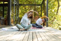 Asian mother and her daughter practicing yoga on terrace in garden. at home in isolation during quarantine lockdown. — Stock Photo