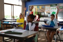 Группа разносторонних учеников поднимает руки в классе в начальной школе. школа и концепция образования — стоковое фото