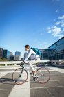 Азійський бізнесмен їздить на велосипеді по міській вулиці з сучасними будівлями на задньому плані. Бізнесмен десь у місті.. — стокове фото