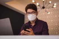 Homme d'affaires asiatique portant un masque facial en utilisant un smartphone et un ordinateur portable dans le hall de l'hôtel. numérique nomade dehors et environ dans la ville pendant covid 19 concept pandémique. — Photo de stock