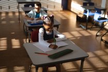 Afroamerikanerin lernt, während sie in der Grundschule auf ihrem Schreibtisch sitzt. Schul- und Bildungskonzept — Stockfoto