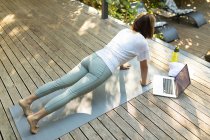 Asiatin praktiziert Yoga mit Laptop auf der Terrasse im Garten. Zuhause in Isolation während der Quarantäne. — Stockfoto