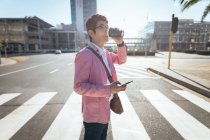 Empresário asiático usando o smartphone bebendo takeaway café cruzando rua da cidade. nômade digital para fora e sobre no conceito da cidade. — Fotografia de Stock