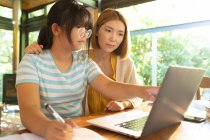 Asian girl using laptop learning online her mum helping her with homework. at home in isolation during quarantine lockdown. — Stock Photo
