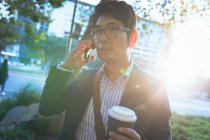Азіатський бізнесмен говорить на смартфоні, тримаючи каву на вулиці міста. Цифровий кочівник і про про про в міській концепції. — стокове фото
