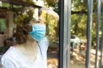 Triste mulher asiática vestindo máscara facial e olhando pela janela. em casa, isoladamente, durante o bloqueio da pandemia e quarentena do covid 19. — Fotografia de Stock