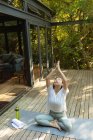 Азиатка практикует йогу с закрытыми глазами на террасе в саду. в доме в изоляции во время карантинной изоляции. — стоковое фото