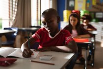 Ein afroamerikanischer Junge lernt, während er in der Grundschule auf seinem Schreibtisch sitzt. Schul- und Bildungskonzept — Stockfoto
