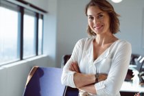 Mulher de negócios caucasiana sorridente de pé de braços cruzados no trabalho. negócio criativo independente em um escritório moderno. — Fotografia de Stock