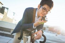 In der Mitte ein asiatischer Geschäftsmann, der auf dem Fahrrad in der Stadtstraße auf dem Smartphone spricht. Digitaler Nomade im Stadtkonzept unterwegs. — Stockfoto