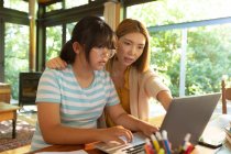 Chica asiática usando el ordenador portátil de aprendizaje en línea de su madre ayudándola con la tarea. en casa en aislamiento durante el bloqueo de cuarentena. - foto de stock