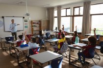 Группа разносторонних учеников поднимает руки в классе в начальной школе. школа и концепция образования — стоковое фото