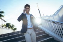 Hombre de negocios asiático hablando en el teléfono inteligente caminando por los escalones en la calle de la ciudad. nómada digital en concepto de ciudad. - foto de stock