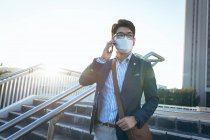 Asiatischer Geschäftsmann mit Gesichtsmaske und Smartphone auf der Straße der Stadt. digitaler Nomade während des Covid 19 Pandemiekonzepts in der Stadt unterwegs. — Stockfoto