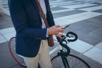 Розрив бізнесмена за допомогою смартфона, що тримає велосипед на міській вулиці. цифровий кочівник і близько в міській концепції . — стокове фото