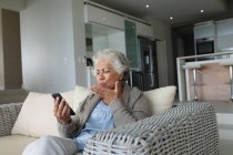 Mixed Race Seniorin sitzt auf dem Sofa und telefoniert per Smartphone. Isolationshaft während der Quarantäne. — Stockfoto