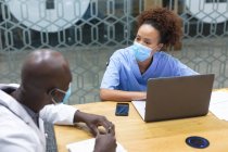 Diverse male doctor and female nurse wearing face masks, using laptop and talking. medicine, health and healthcare services during coronavirus covid 19 pandemic. — Stock Photo
