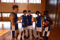 Mannigfaltige männliche Basketballmannschaft und Trainer diskutieren im Gedränge über Spieltaktik. Basketball, Sporttraining auf einem Indoor-Court. — Stockfoto
