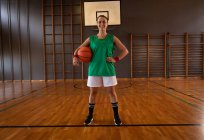 Retrato de una jugadora de baloncesto caucásica sosteniendo la pelota. baloncesto, entrenamiento deportivo en una cancha cubierta. - foto de stock