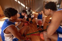 Equipe masculine diversifiée de basket-ball et entraîneur dans huddle discuter des tactiques de jeu. basket-ball, entraînement sportif sur un terrain intérieur. — Photo de stock