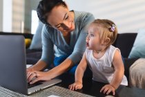Sorrindo mãe caucasiana olhando para seu bebê usando laptop enquanto trabalhava em casa. maternidade, amor e conceito de cuidado do bebê — Fotografia de Stock