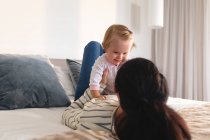 Ritratto di madre caucasica che gioca con il suo bambino sdraiato sul letto a casa. maternità, amore e concetto di cura del bambino — Foto stock
