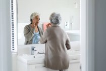 Eine Seniorin mit gemischter Rasse betrachtet ihr Spiegelbild im Spiegel. Isolationshaft während der Quarantäne. — Stockfoto