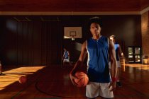 Portrait eines Basketballspielers gemischter Rasse mit einer Mannschaft im Hintergrund. Basketball, Sporttraining auf einem Indoor-Court. — Stockfoto