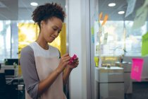 Gemischte Geschäftsfrau, die Notizen auf Glasplatten macht und lächelt. Arbeit in einem unabhängigen kreativen Unternehmen. — Stockfoto